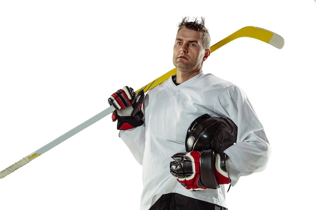 Jugador de hockey masculino joven con el palo en la cancha de hielo y pared blanca