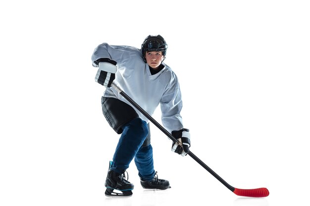 Jugador de hockey masculino joven con el palo en la cancha de hielo y pared blanca