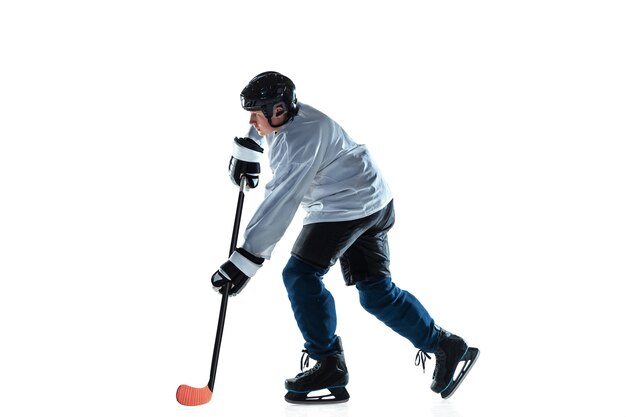 Jugador de hockey masculino joven con el palo en la cancha de hielo y pared blanca