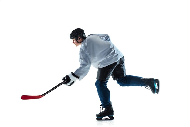 Jugador de hockey masculino joven con el palo en la cancha de hielo y pared blanca