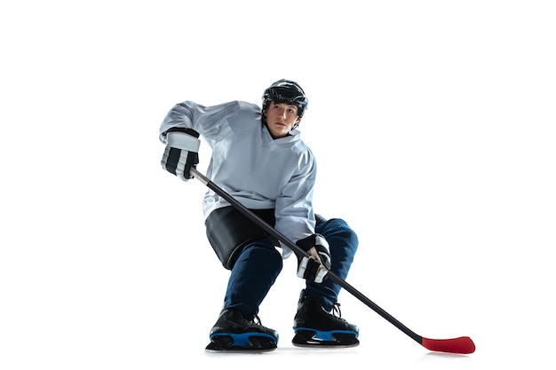 Jugador de hockey masculino joven con el palo en la cancha de hielo y pared blanca