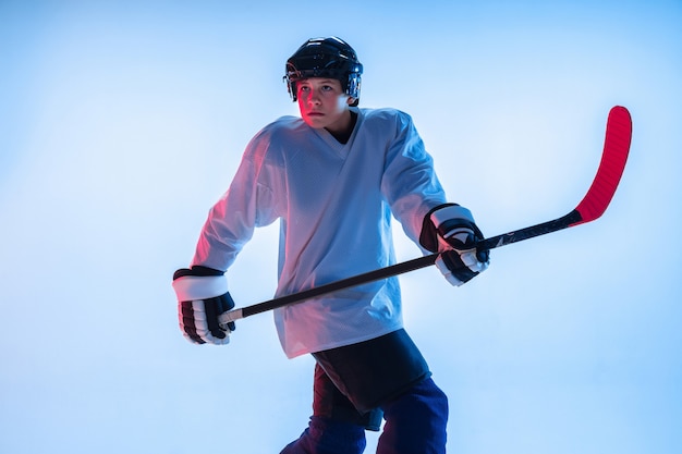 Jugador de hockey masculino joven con el palo en la pared azul en luz de neón