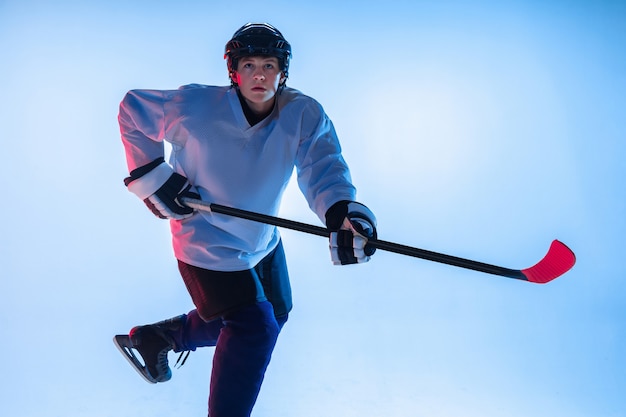 Jugador de hockey masculino joven con el palo en la pared blanca en luz de neón