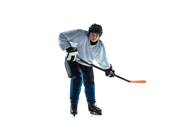 Jugador de hockey masculino joven serio con el palo en la cancha de hielo y la pared blanca