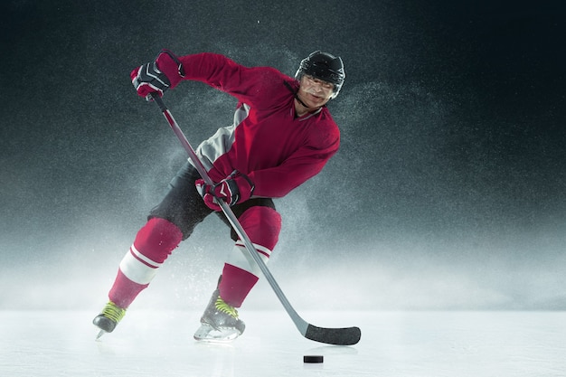 Jugador de hockey masculino con el palo en la cancha de hielo y pared oscura
