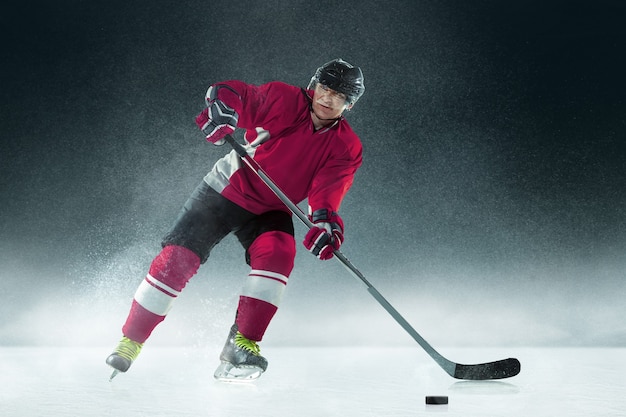 Jugador de hockey masculino con el palo en la cancha de hielo y pared oscura