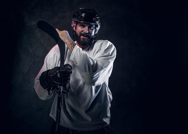 El jugador de hockey profesional con casco posa con un palo de hockey en un estudio fotográfico.