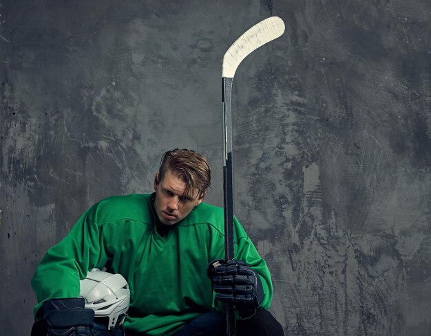 El jugador de hockey con uniforme protector negro sostiene un palo de hockey sobre un fondo gris.