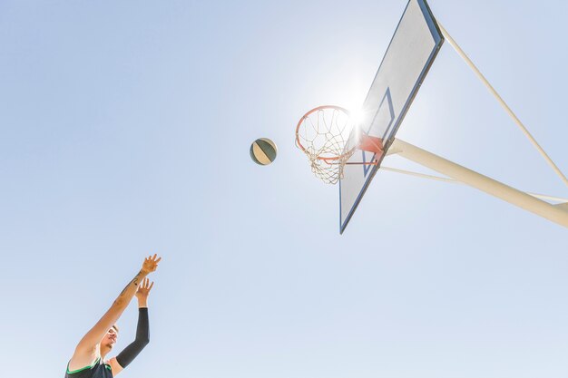 Un jugador masculino que lanza baloncesto en el aro contra el cielo azul claro