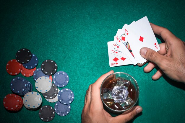 Jugador de póker con vaso de whisky y tarjeta de escalera real en la mesa de póquer