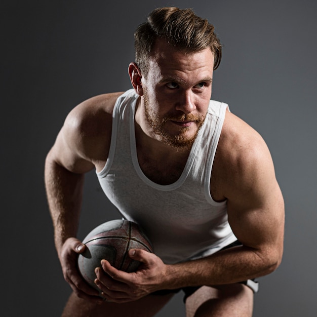 Jugador de rugby masculino guapo sosteniendo la bola y posando