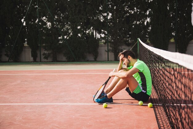 Jugador de tenis apoyado contra red en frustración
