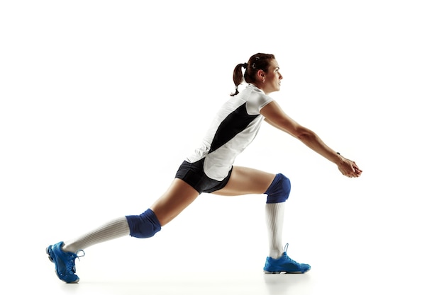 Jugador de voleibol femenino joven aislado en la pared blanca. Mujer en equipamiento deportivo y zapatos o zapatillas de deporte entrenando y practicando. Concepto de deporte, estilo de vida saludable, movimiento y movimiento.