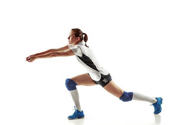 Jugador de voleibol femenino joven aislado sobre fondo blanco de estudio. Mujer en equipamiento deportivo y zapatos o zapatillas de deporte entrenando y practicando. Concepto de deporte, estilo de vida saludable, movimiento y movimiento.