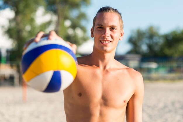 Jugador de voleibol masculino sin camisa sonriente en la playa sosteniendo la bola