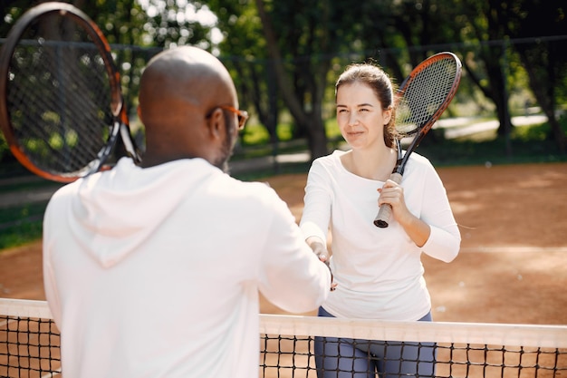 Foto gratuita los jugadores de tenis finalizan el juego. hombre negro y amiga dando apretón de manos después del juego cerca de la red.