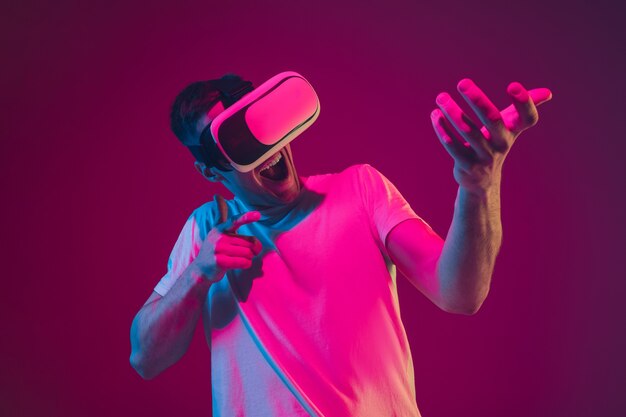 Jugar con realidad virtual, disparar, conducir. Retrato de hombre caucásico en estudio rosa-violeta en luz de neón.