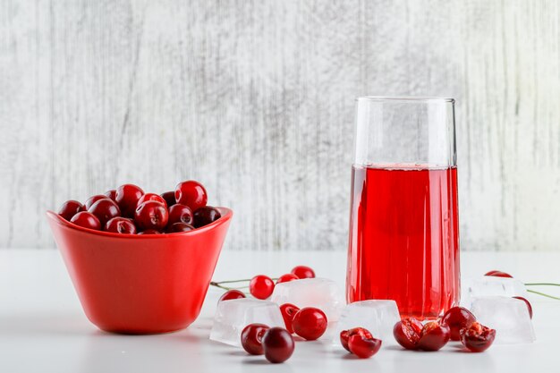 Jugo de cereza con cerezas, cubitos de hielo en un vaso sobre blanco