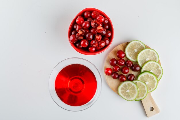 Jugo de cereza con cerezas, rodajas de limón en un vaso sobre blanco