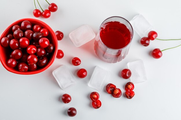 Jugo de cereza en un vaso con cerezas, cubitos de hielo en blanco