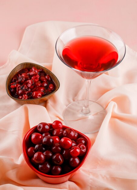 Jugo de cereza en un vaso con cerezas, mermelada vista de ángulo alto en rosa y textil