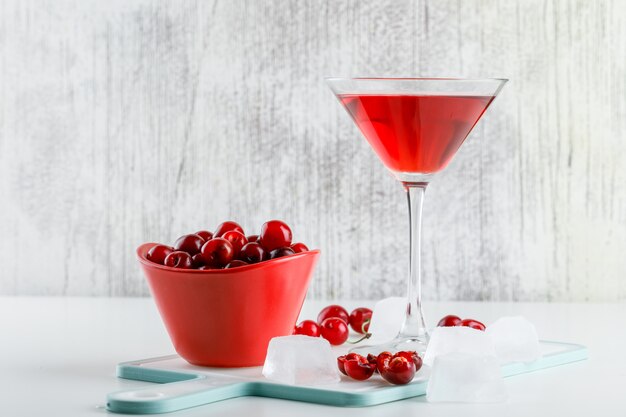 Jugo de cereza en un vaso con cerezas, vista lateral de la tabla de cortar en blanco y sucio