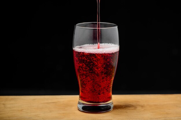 Jugo de cereza vertiendo en vidrio sobre escritorio de madera