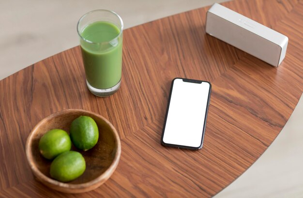 Jugo de desintoxicación y teléfono inteligente con pantalla en blanco sobre una mesa de madera