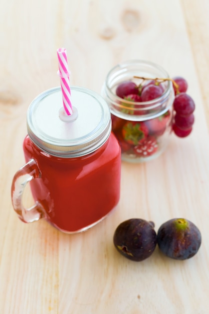 Jugo de fresa, higos y uvas sobre fondo de madera.