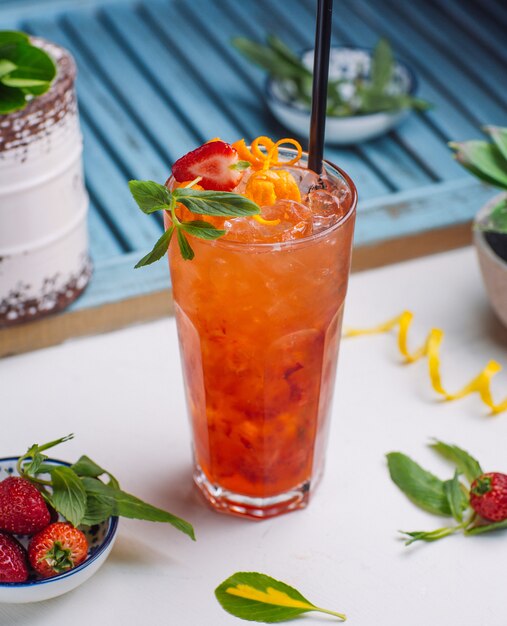 jugo de fresa y naranja con cubitos de hielo, ralladura de naranja, trozo de fresa en vaso