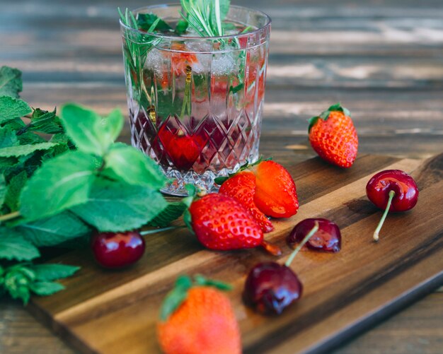 Jugo fresco; hoja de menta cerca de fresas y cerezas en la tabla de cortar