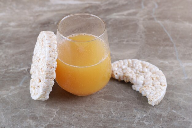 Jugo de fruta junto a tortas de arroz inflado, sobre la superficie de mármol