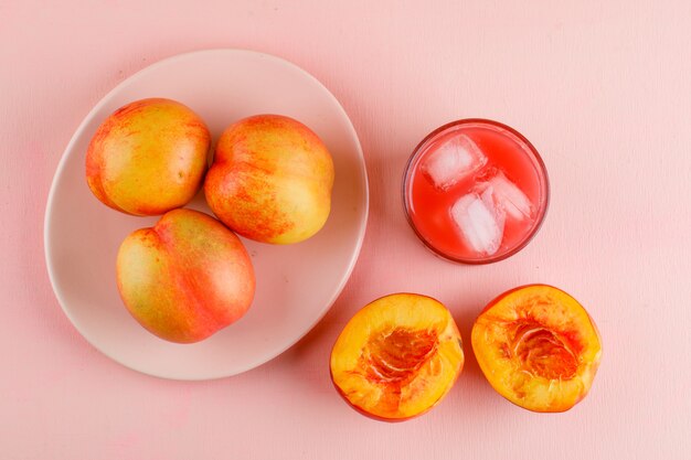 Jugo helado en un vaso con nectarinas planas sobre una superficie rosa