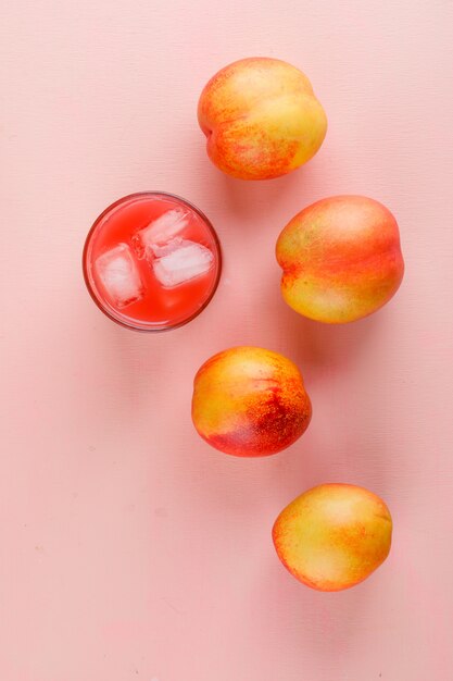 Jugo helado en un vaso con nectarinas vista superior sobre una superficie rosa