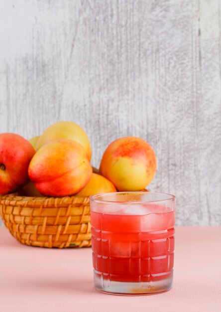 Jugo helado en un vaso con vista lateral de nectarinas en la pared rosada y sucia