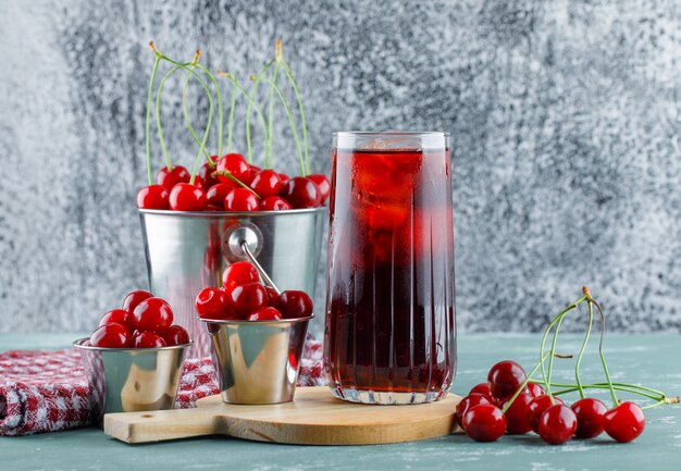 Jugo en una jarra con cereza, tabla de cortar, vista lateral de toalla de cocina