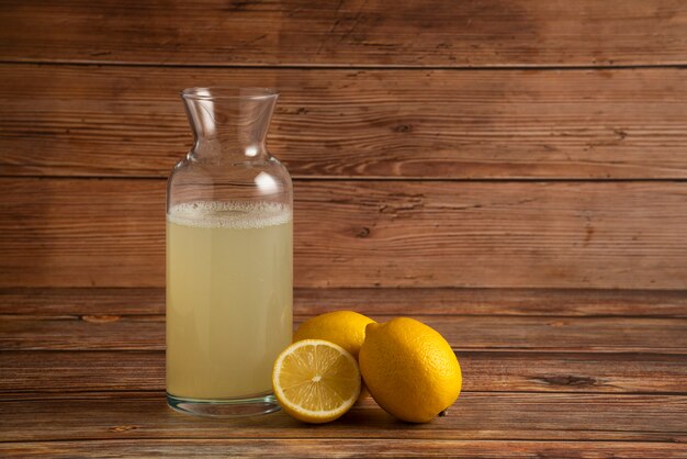 Jugo de limón en el recipiente de vidrio con frutas sobre la mesa de madera