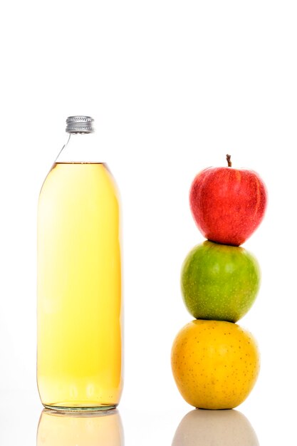 Jugo de manzana en botella de vidrio y tres manzanas maduras