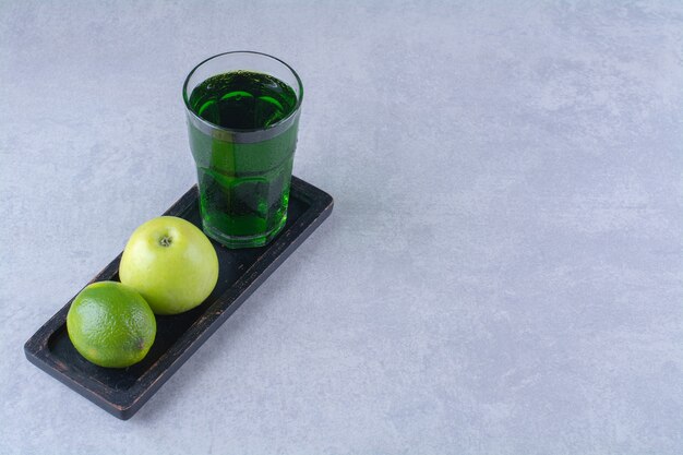 Jugo de manzana, limón y manzana en una placa de madera sobre mesa de mármol.
