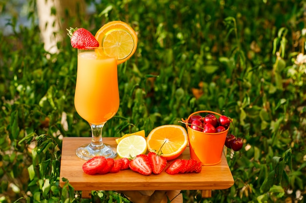 Jugo de naranja con cítricos, fresa, cereza, tabla de cortar en una copa, vista lateral.