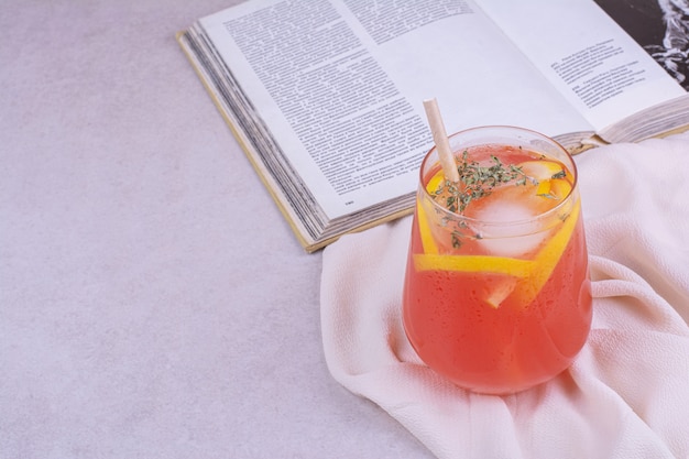 Jugo de naranja con rodajas de frutas y especias en mesa blanca.