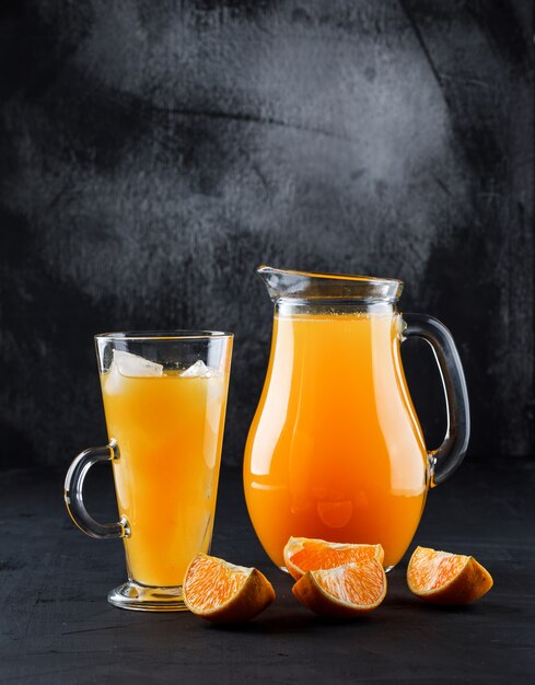 Jugo de naranja en vaso de vidrio y jarra con rodajas de naranja