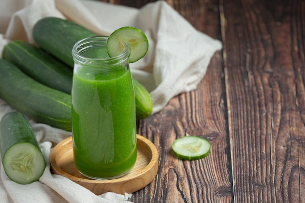 Jugo de pepino fresco en un frasco sobre fondo de madera oscura.