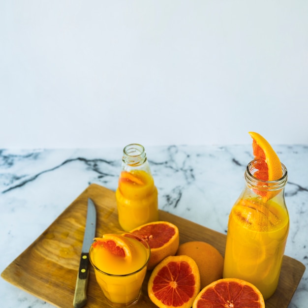 Jugo de pomelo casero en vidrio y botellas en una tabla de cortar con un cuchillo afilado