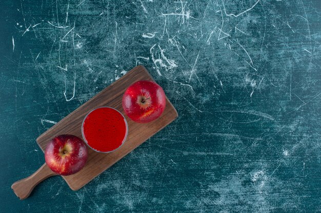 Jugo rojo y manzana en el tablero, sobre fondo azul. Foto de alta calidad