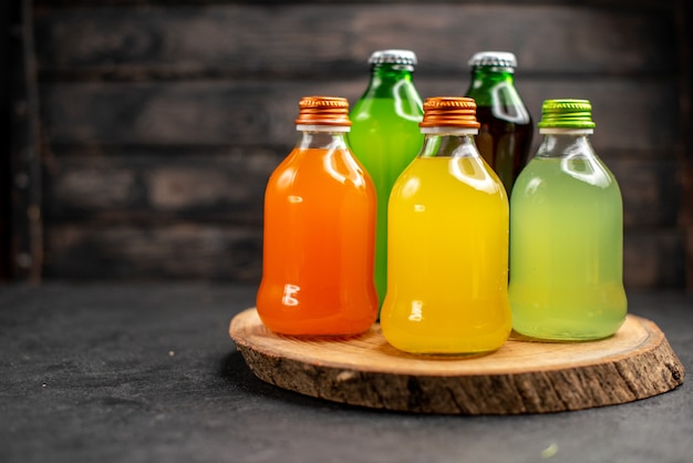 Jugos de vista frontal de diferentes colores en botellas sobre tablero de madera sobre superficie de madera oscura.