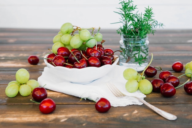 Jugosas cerezas y uvas en un tazón en el escritorio de madera