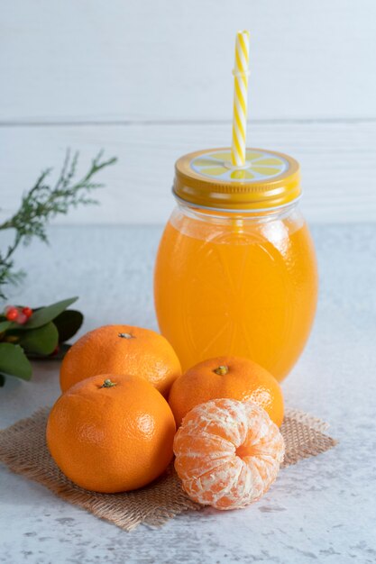 Jugosas frutas de mandarina y tarro de jugo de naranja en la mesa de piedra