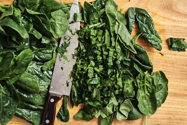 Jugosas hojas de espinaca picadas en una tabla de cortar de madera. El cuchillo del cocinero se encuentra sobre la mesa, vista superior. Alimentos orgánicos y saludables. La idea de hacer el desayuno