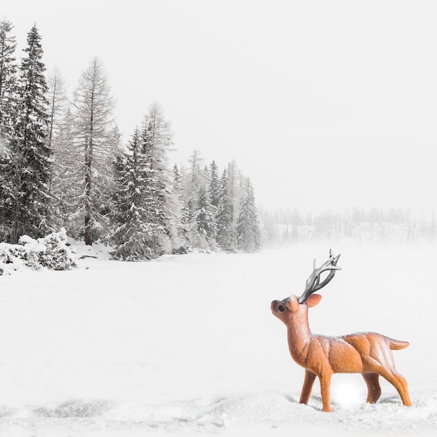 Juguete de ciervo entre campo con árboles en la nieve.